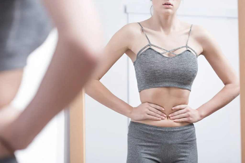 a woman standing in front of a mirror with her hands on her stomach