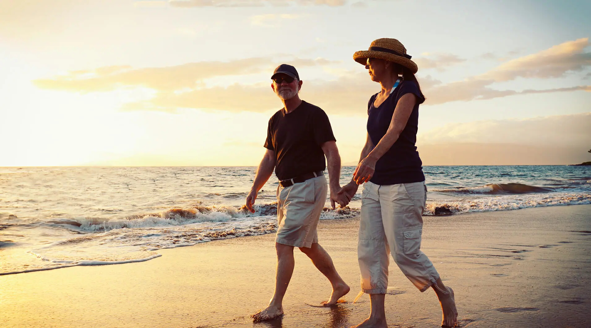 Elderly Couple Holding Hands and Walking on Beach at Sunset | Synergy Wellness Center - Bakersfield CA