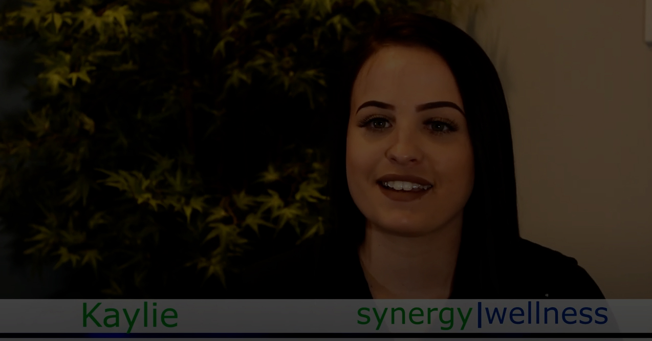 a woman is smiling in front of a sign that says synergy wellness