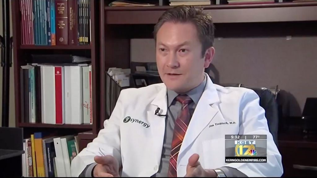 a doctor in a white lab coat with the word synergy on it being interviewed